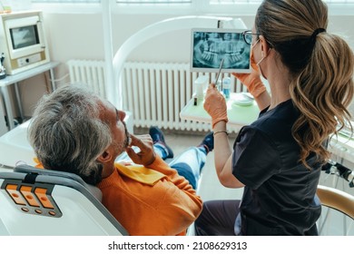 Unrecognizable Female Dentist Explaining Teeth X-ray Using a Digital Tablet to Worried Mature Patient at Dentist's Office - Powered by Shutterstock