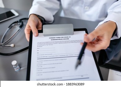 Unrecognizable Female Doctor Offering A Pen To Sign The Coronavirus Vaccine Consent Form