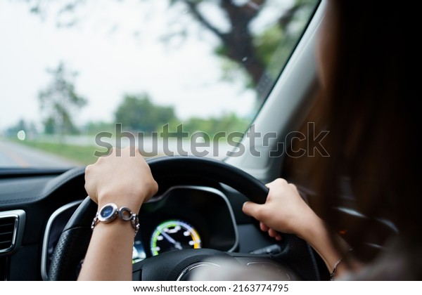 Unrecognizable female driver using left hand\
grabs on the steering wheel while driving on the road, woman\
driving a modern electric car EV in beautiful sunlight on the road.\
Safety driving\
concept.