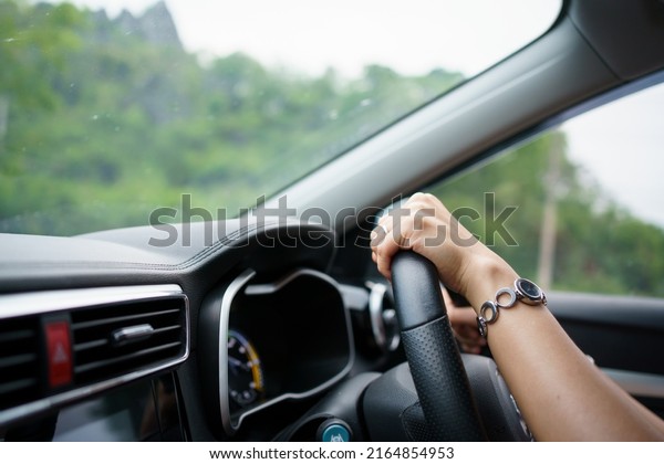 Unrecognizable female driver using left hand
grabs on the steering wheel while driving on the road, woman
driving a modern electric car EV in beautiful sunlight on the road.
Safety driving
concept.
