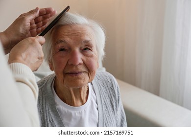 Unrecognizable female expressing care towards an elderly lady, brushing her hair with a comb. Granddaughter helping granny with a haircut. Family values concept. lose up, copy space, background. - Powered by Shutterstock