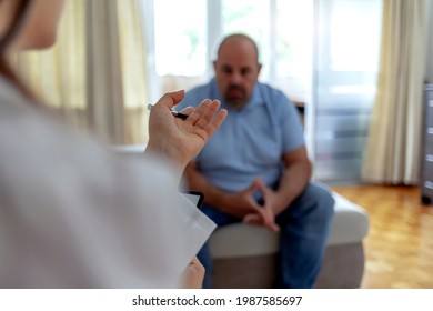 Unrecognizable Female Mental Health Professional Takes Notes While Discussing A Male Patient's Issues. The Patient Is Sitting Across From The Mental Health Professional. Focus On Hands. Copy Space.