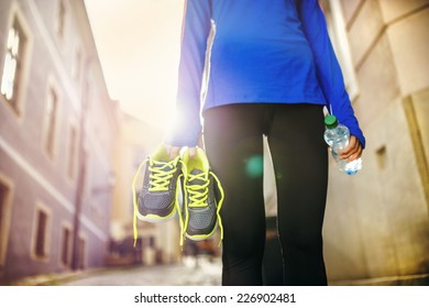 Unrecognizable Female Runner Carrying Her Running Shoes And Bottle Of Water In Old City Center