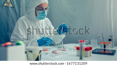 Unrecognizable female scientist with bacteriological protection suit doing research in the laboratory