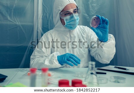 Unrecognizable female scientist with bacteriological protection suit examining a petri dish in the laboratory