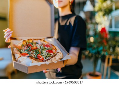 Unrecognizable Female Staff Waiter Showing Open Box With Freshly Baked Pizza Indoor With Modern Interior Of Pizza Shop Or Cafeteria On Blurred Background. Take Away Only Concept.