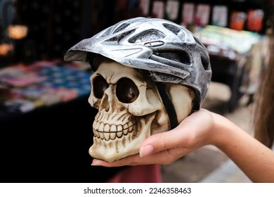 Unrecognizable female tourist demonstrating artificial human skull with bicycle helmet while visiting street market - Shutterstock ID 2246358463