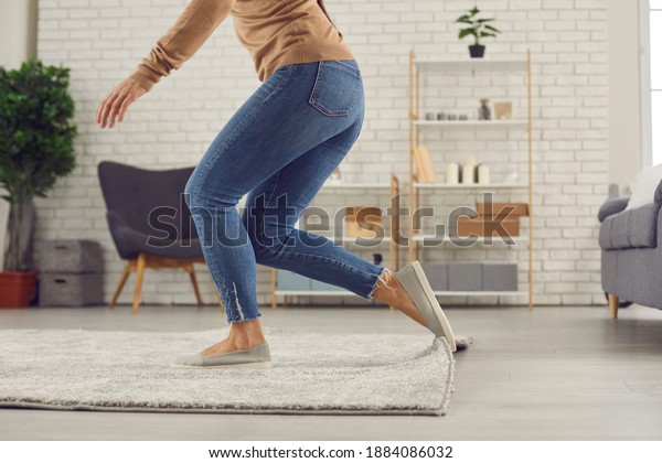 Unrecognizable female trips over rug. Clumsy\
faceless woman in uncomfortable shoes stumbles on rug in\
living-room and is about to fall on floor. Domestic accidents and\
getting injured at home\
concept