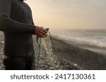 Unrecognizable fisherman in wetsuit collecting fish from a net standing on the beach