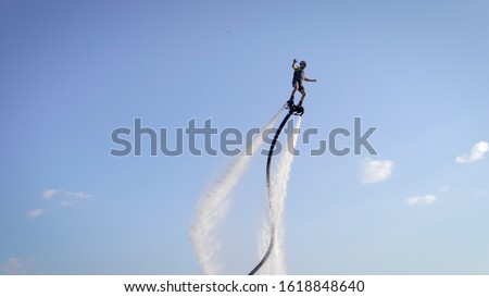 Unrecognizable flyboarder connected by long hose riding and balancing on background of blue sky