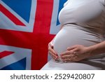 Unrecognizable future mother expecting baby on Great Britain national flag background. Pregnant woman touching belly. Demography crisis, population problems in England. High quality