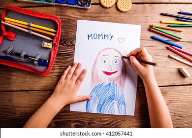 Unrecognizable girl drawing picture of her mother. Wooden backgr