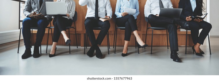 Unerkennbare Gruppe verschiedener Geschäftsleute, die in Stühlen an einem Bürorezeptionstisch sitzen und darauf warten, befragt zu werden