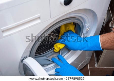 An unrecognizable hand cleans accumulated dirt in the washing machine with a yellow cloth