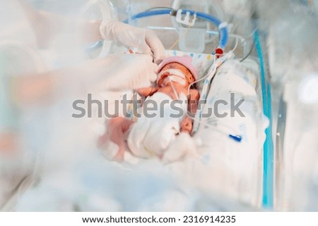 Unrecognizable hand in gloves of nurse or doctor taking care of premature baby placed in a medical incubator. Neonatal intensive care unit in hospital.