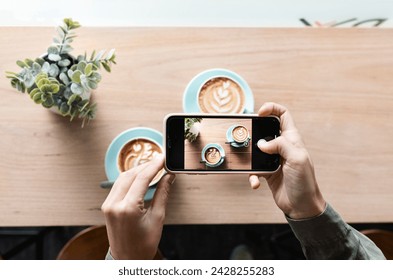 Unrecognizable hands taking a aerial shot of two cups of coffee in a hipster cafe. She use a smartphone. Latte art on the foamy flat white. - Powered by Shutterstock