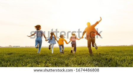 Unrecognizable happy   parents with daughters in casual clothes running back with holding hands while enjoying time together on green meadow in summer evening
