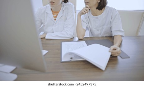 Unrecognizable Healthcare Caucasian colleagues collaborating on a review of medical records at an office workstation. - Powered by Shutterstock