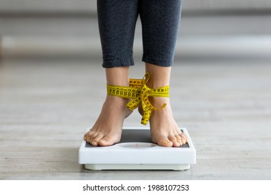 Unrecognizable Indian woman standing on scales with tied feet, checking her weight. Closeup view of millennial lady obsessed with idea of slimming, suffering from eating disorder