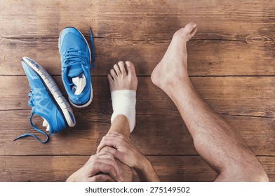 Unrecognizable injured runner sitting on a wooden floor background
