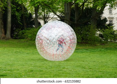 Unrecognizable Kid Zorbing Inside Transparent Plastic Zorb Ball In Park