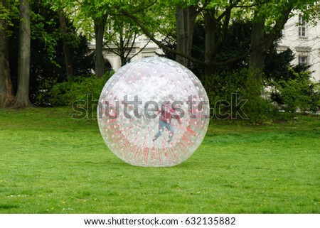 unrecognizable kid zorbing inside transparent plastic zorb ball in park