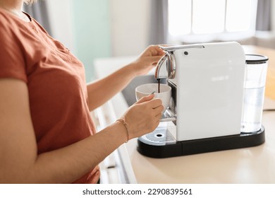 Unrecognizable Lady Using Coffee Machine In Kitchen At Home, Young Female Holding Cup And Pouring Caffeine Drink With Modern Appliance, Millennial Woman Enjoying Morning Beverage, Cropped Image - Powered by Shutterstock