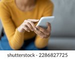 Unrecognizable Lady Using Modern Smartphone While Sitting On Couch At Home, Closeup Shot Of Female Hands Holding Cellphone, Young Woman Browsing App On Mobile Phone Or Shopping Online, Cropped