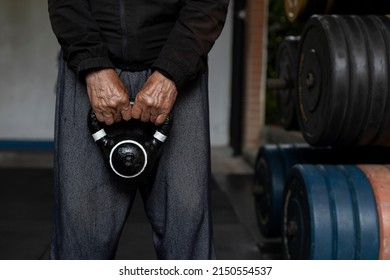 Unrecognizable Latin American Senior Male Holding A Kettlebell With Both Hands During His Rehabilitation And Therapy Workouts At The Gym. Healthy Lifestyle Concept.