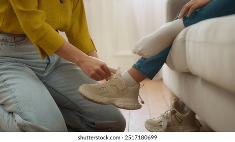 Unrecognizable loving Caucasian woman mother carer female hands lacing ties shoelaces unknown little girl daughter helping tying sneakers child kid in living room at morning. Upbringing family support - Powered by Shutterstock