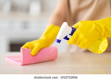 Unrecognizable maid in rubber gloves cleaning countertop at kitchen, closeup of hands with detergent and rag. Professional sanitary service worker doing house cleanup, wiping table