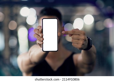 Unrecognizable Male Athlete Holding And Pointing At Blank Smartphone While Standing In Gym, Sportsman Recommending Fitness App, Showing Copy Space For Advertisement, Selective Focus, Mockup