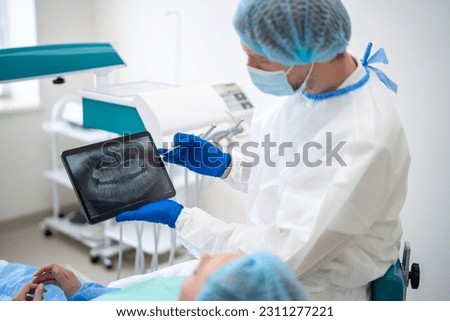 Unrecognizable male dentist in medical uniform showing x ray image of teeth while consulting anonymous female client in stomatological chair [[stock_photo]] © 
