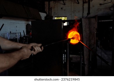 Unrecognizable male glassmith putting metal blowpipe with heated glass in form of hookah vase on tip into annealer furnace while working at factory - Powered by Shutterstock