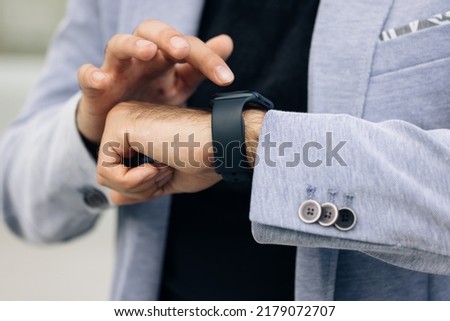 Unrecognizable male hands using smart watch. Businessman uses a smartwatch on his hand and keeps track of the time on the display. Close up of businessman checks smartwatch. Jacket formal wear