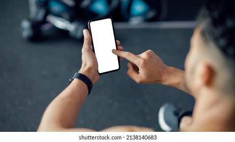 Unrecognizable Male Using Cellphone With White Screen At Gym, Mockup Image Of Sporty Man Browsing Mobile App On Blank Phone While Relaxing After Training In Sport Club, Over Shoulder View