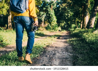 Unrecognizable Man With Backpack And Boots Holding A Camera In Front Of A Path In A Forest, Nature Travel And Hiking Concept.