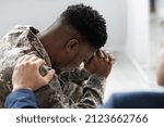 Unrecognizable man in blue suit government official, social worker or psychologist placing hand on upset black man in camouflage uniform soldier shoulder, side view, copy space