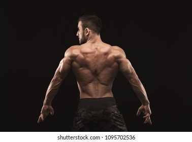 Unrecognizable man bodybuilder shows strong hands and back muscles, athletic trapezius. Low key, studio shot on black background.