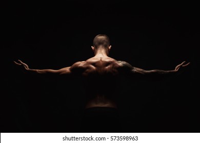 Unrecognizable man bodybuilder shows strong hands and neck muscles, athletic trapezius. Low key, studio shot on black background.