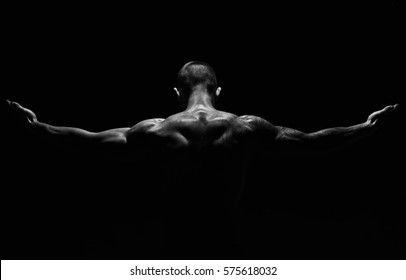 Unrecognizable man bodybuilder shows strong hands and neck muscles, athletic trapezius. Black and white, monochrome studio shot on black background.