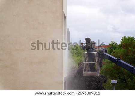 Unrecognizable man cleaning facade surface from lifting platform with high pressure stream of water