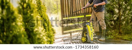Unrecognizable man cleaning a wooden gate with a power washer. High pressure water cleaner used to DIY repair garden gate. Web banner.