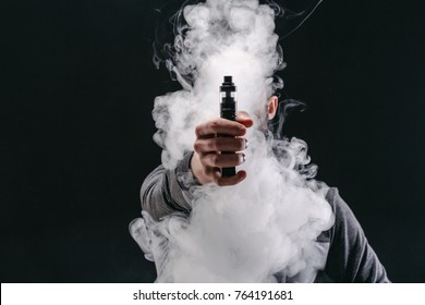 Unrecognizable man in the cloud of vape smoke. Guy smoking e-cigarette to quit tobacco. Vapor and alternative nicotine free smoking concept, copy space