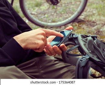 Unrecognizable man cyclist searches GPS coordinates on the mobile phone in the forest