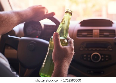 An unrecognizable man drinking beer while driving car. Concepts of driving under the influence, drunk driving or impaired driving
