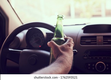 An unrecognizable man drinking beer while driving car. Concepts of driving under the influence, drunk driving or impaired driving