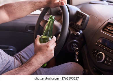 An unrecognizable man drinking beer while driving car. Concepts of driving under the influence, drunk driving or impaired driving