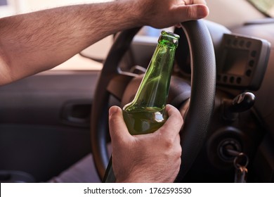 An unrecognizable man drinking beer while driving car. Concepts of driving under the influence, drunk driving or impaired driving
