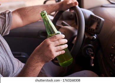 An unrecognizable man drinking beer while driving car. Concepts of driving under the influence, drunk driving or impaired driving